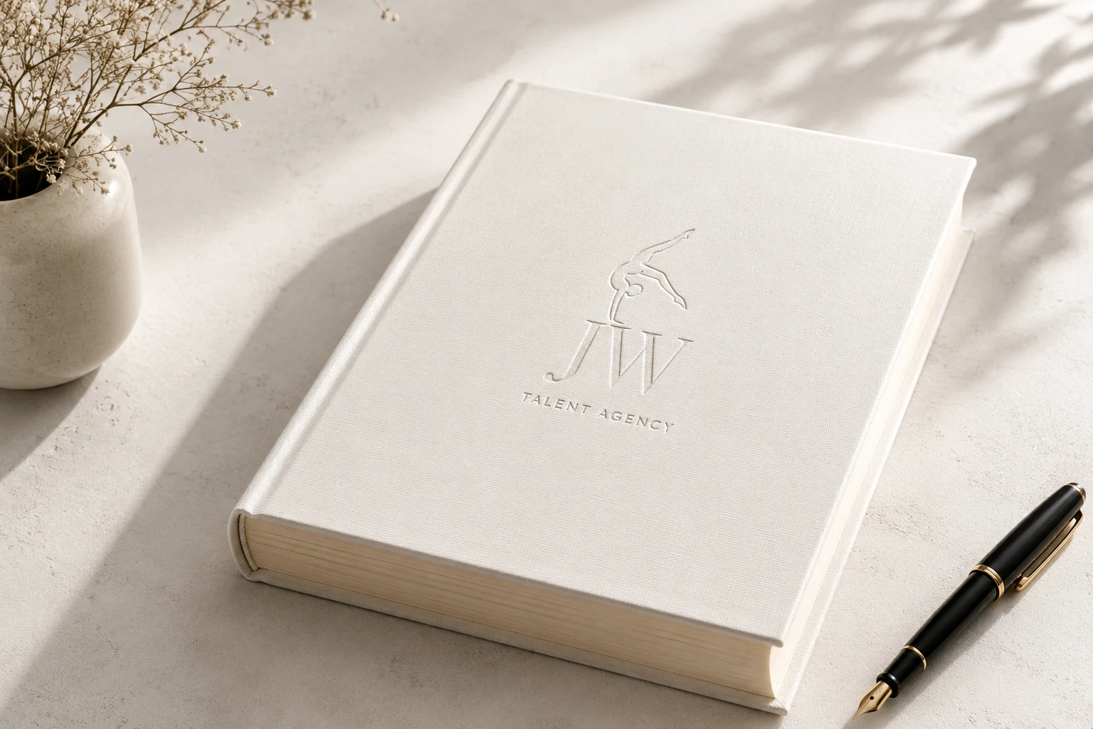 A closed white linen JW Talent Agency book beside a fountain pen